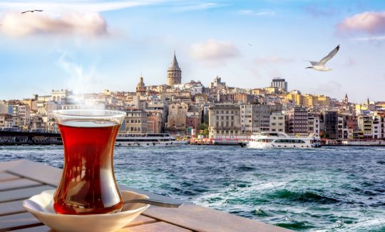a cup of turkish tea in a traditional glass against the background of the golden horn and the galata tower in istanbul